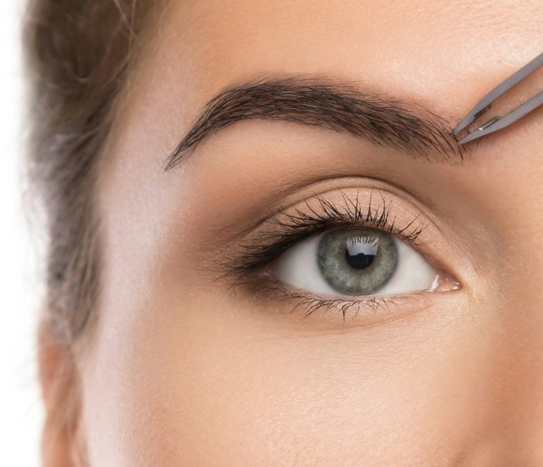 Close-up of female face and eyebrow with tweezers