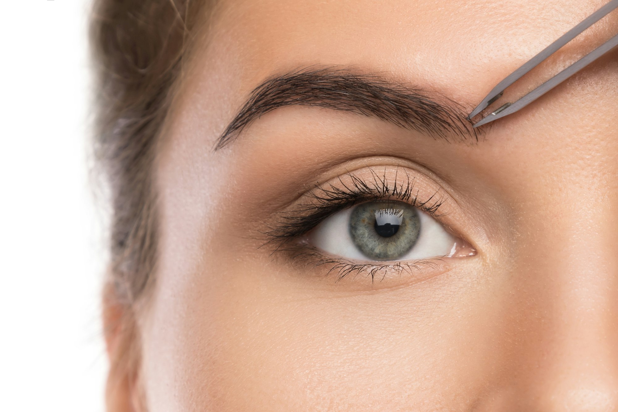 Close-up of female face and eyebrow with tweezers